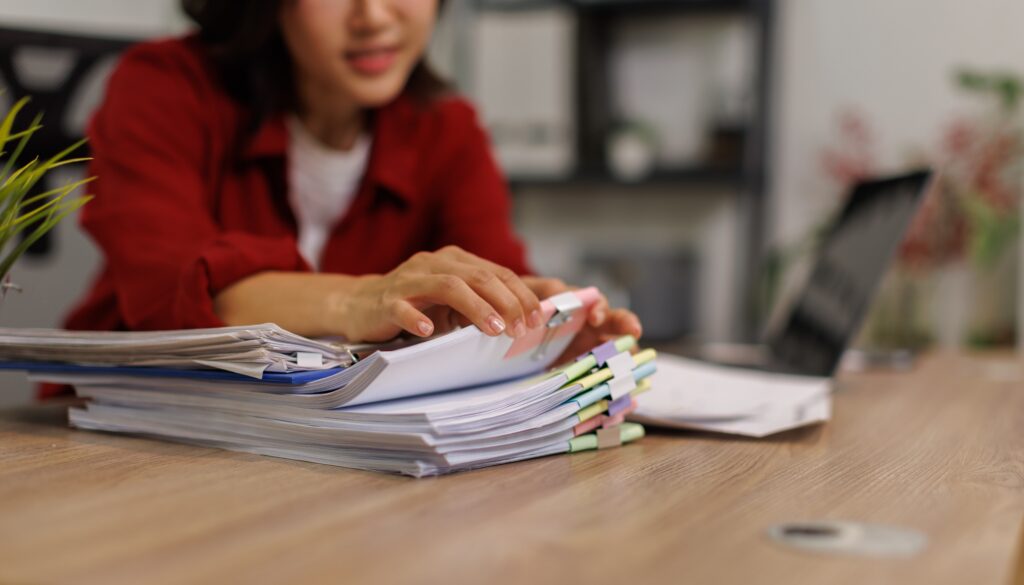 Woman flipping through a pile of papers, compiling a manual report